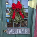 Fresh-cut fir and cedar holiday door swag with red wired bow hanging on a front door